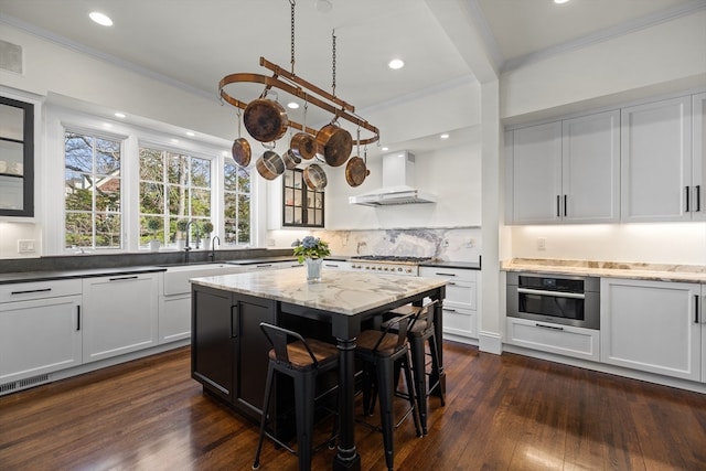 kitchen featuring wall chimney exhaust hood, oven, dark wood-type flooring, and a kitchen island