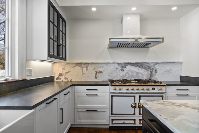 kitchen with backsplash, double oven range, wall chimney range hood, white cabinetry, and dark hardwood / wood-style flooring