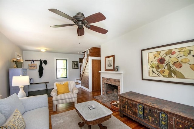 living room with a brick fireplace, dark wood-type flooring, and ceiling fan