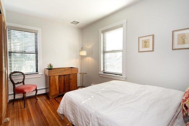 bedroom with wood-type flooring, baseboard heating, and multiple windows