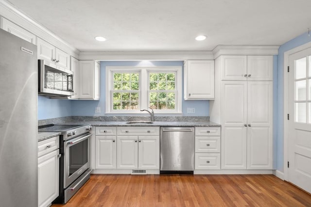 kitchen featuring stainless steel appliances, a sink, light wood-style flooring, white cabinetry, and light stone countertops