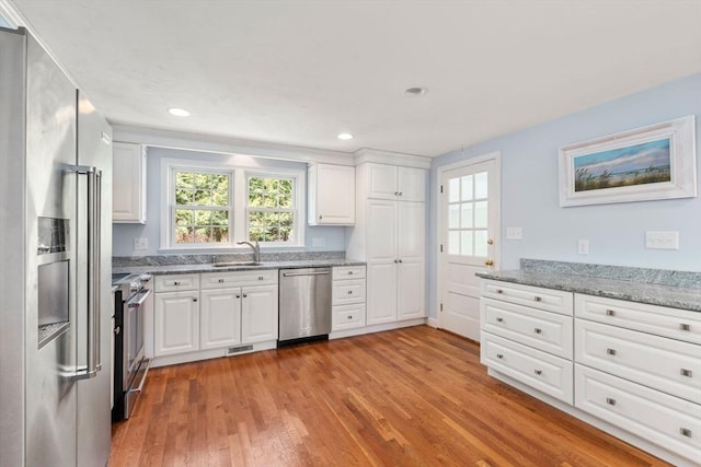 kitchen featuring stainless steel appliances, light wood finished floors, white cabinetry, a sink, and recessed lighting