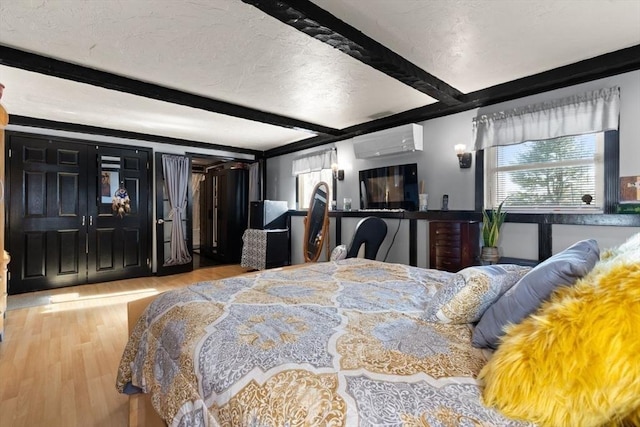 bedroom featuring beamed ceiling, a textured ceiling, a wall unit AC, and light hardwood / wood-style flooring