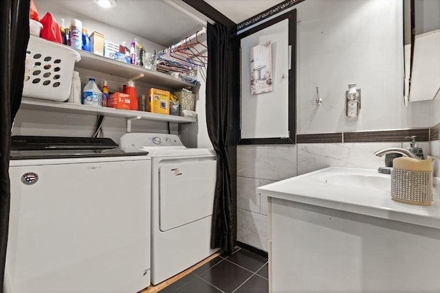 laundry area featuring dark tile patterned floors, washing machine and dryer, sink, and tile walls