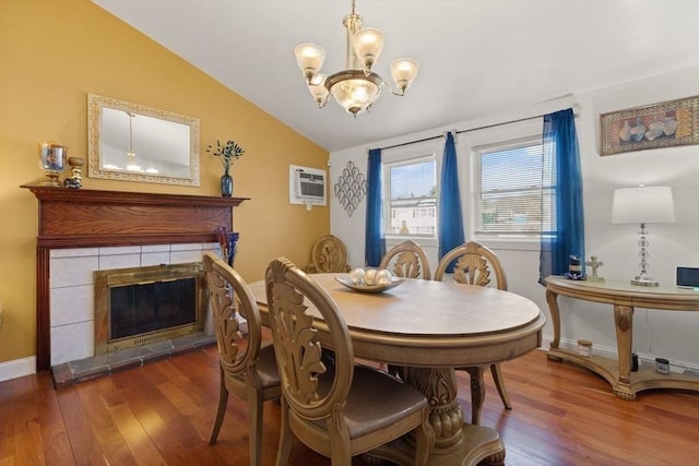dining area featuring lofted ceiling, a chandelier, an AC wall unit, dark hardwood / wood-style floors, and a tiled fireplace