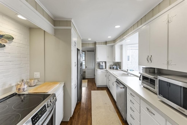 kitchen with sink, dark wood-type flooring, appliances with stainless steel finishes, white cabinets, and ornamental molding