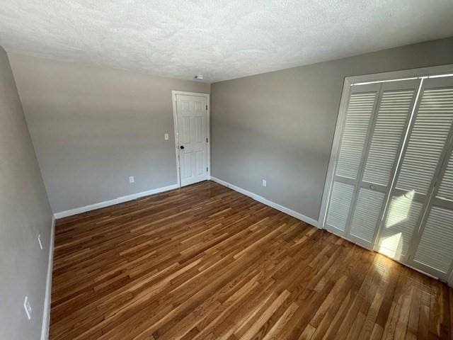 unfurnished bedroom with a textured ceiling, dark hardwood / wood-style flooring, and a closet