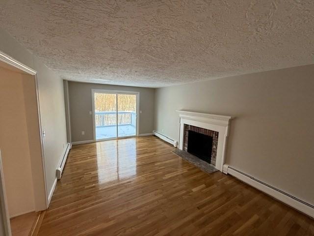 unfurnished living room featuring hardwood / wood-style floors, a brick fireplace, and a baseboard heating unit