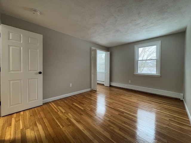 spare room featuring baseboard heating, light hardwood / wood-style flooring, and a textured ceiling