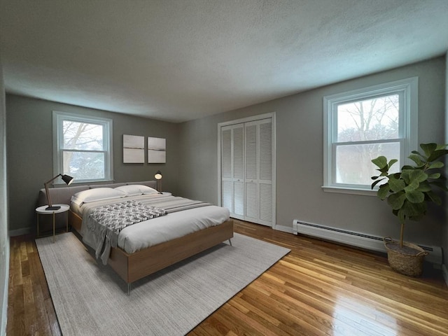 bedroom with baseboard heating, a closet, multiple windows, and light wood-type flooring