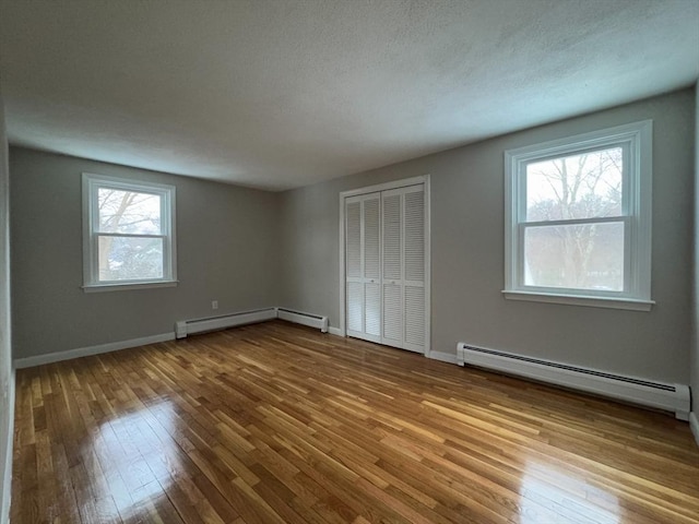 unfurnished bedroom with a baseboard heating unit, a textured ceiling, light wood-type flooring, and a closet