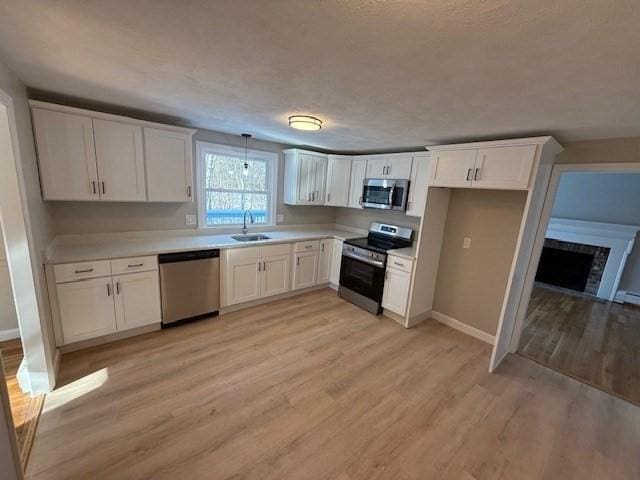 kitchen featuring white cabinetry, sink, hanging light fixtures, light hardwood / wood-style floors, and stainless steel appliances