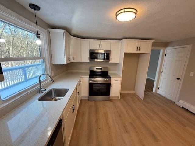 kitchen featuring pendant lighting, sink, white cabinetry, stainless steel appliances, and light stone countertops