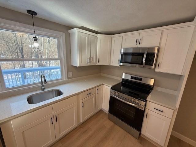 kitchen featuring pendant lighting, sink, stainless steel appliances, light hardwood / wood-style floors, and white cabinets