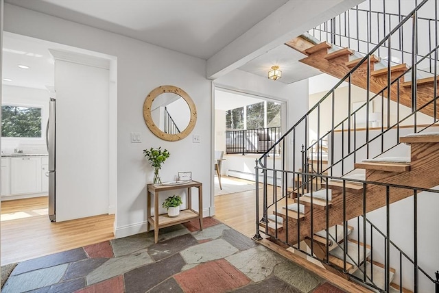 entryway with stone tile flooring, a baseboard heating unit, stairs, and baseboards