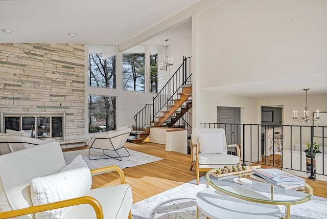 living room featuring wood finished floors, a high ceiling, a stone fireplace, stairs, and a chandelier