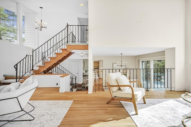 living area with stairs, an inviting chandelier, light wood-style flooring, and a towering ceiling