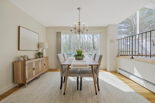 dining space featuring a baseboard heating unit, baseboards, an inviting chandelier, and light wood finished floors