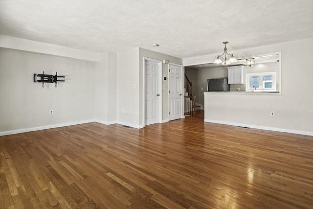 unfurnished living room with a textured ceiling, a chandelier, baseboards, and dark wood-type flooring