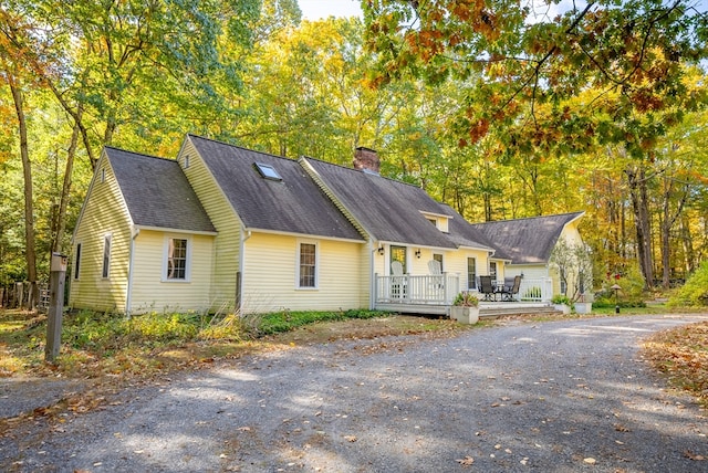 view of front of property featuring a deck, roof with shingles, and a chimney