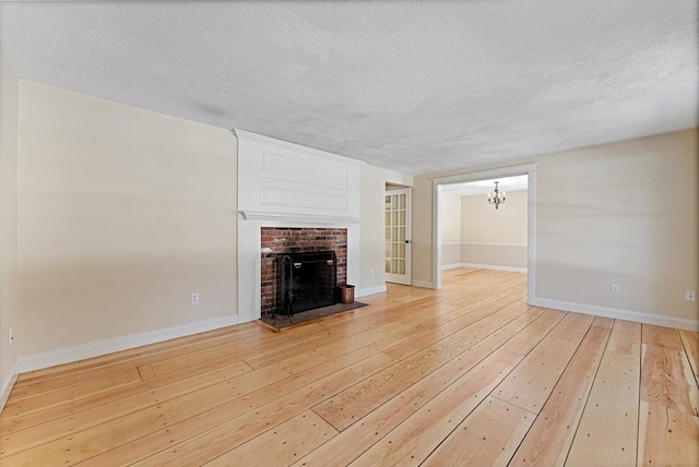 unfurnished living room with light wood-type flooring, a textured ceiling, baseboards, a brick fireplace, and a chandelier