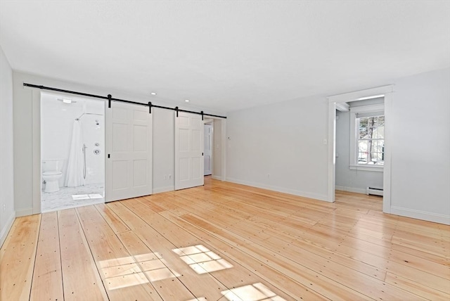 spare room featuring a barn door, baseboards, light wood-type flooring, and baseboard heating