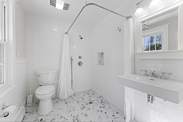 bathroom with baseboard heating, toilet, tile walls, and tiled shower