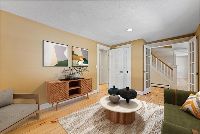 living area featuring baseboards, stairway, a baseboard radiator, a textured ceiling, and wood-type flooring