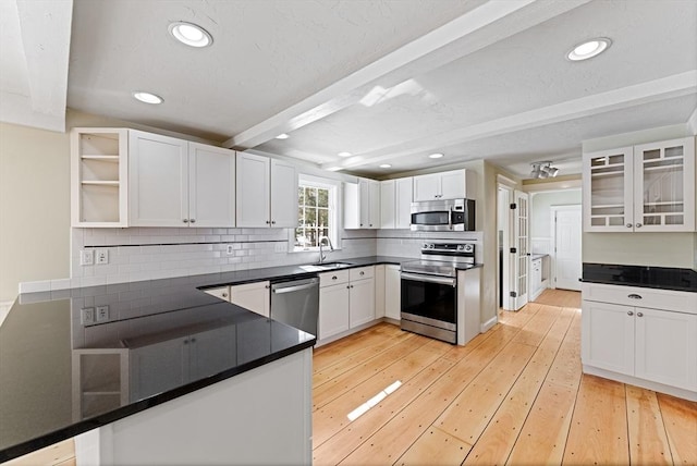 kitchen with beam ceiling, white cabinets, stainless steel appliances, and dark countertops