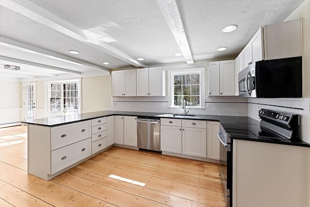 kitchen with beam ceiling, dark countertops, stainless steel appliances, a peninsula, and light wood finished floors