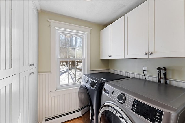 clothes washing area with a wainscoted wall, cabinet space, washer and dryer, and a textured ceiling