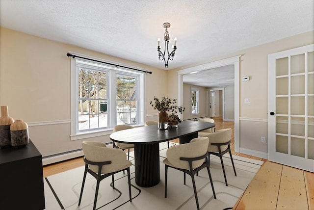 dining area with a baseboard heating unit, baseboards, light wood-type flooring, an inviting chandelier, and a textured ceiling