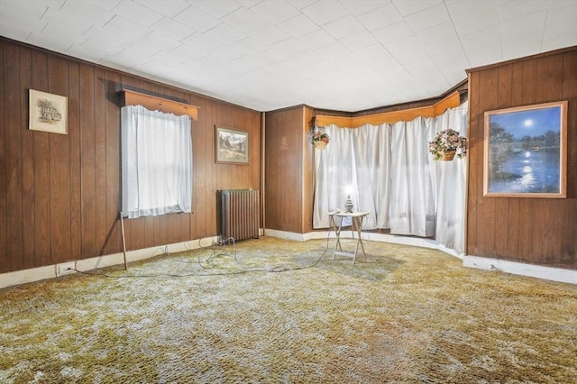 carpeted spare room featuring radiator, wood walls, and baseboards