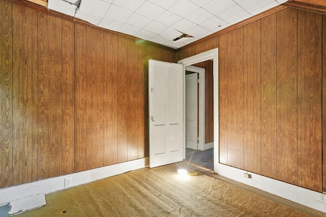carpeted empty room featuring wood walls
