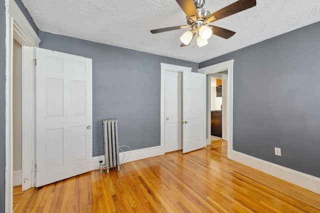 unfurnished bedroom featuring ceiling fan, a textured ceiling, radiator, baseboards, and wood finished floors