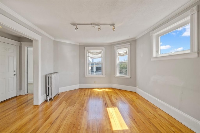 empty room with track lighting, radiator, baseboards, light wood-type flooring, and ornamental molding