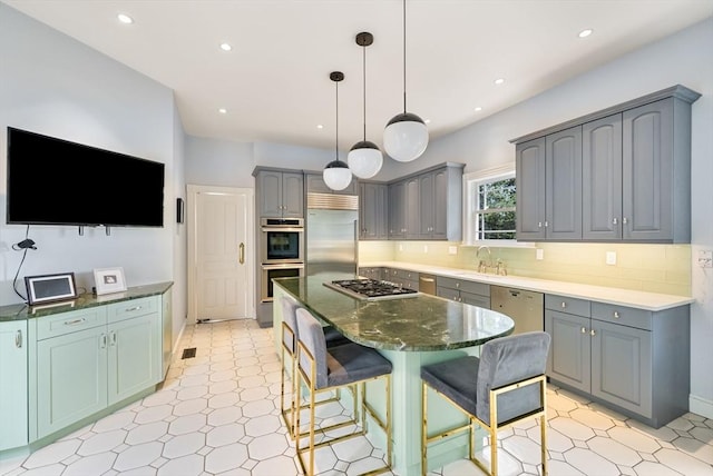 kitchen with stainless steel appliances, a sink, a center island, gray cabinets, and decorative backsplash