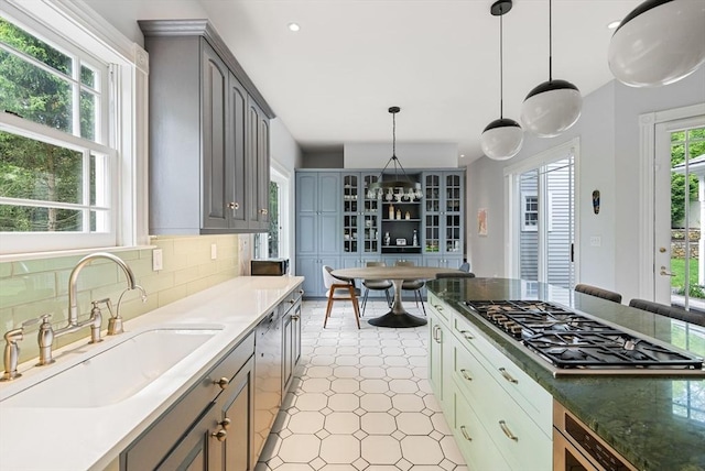 kitchen with stainless steel gas stovetop, a sink, gray cabinets, hanging light fixtures, and tasteful backsplash