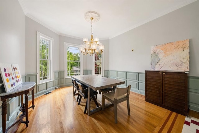 dining area with a chandelier, light wood-style floors, ornamental molding, wainscoting, and a decorative wall