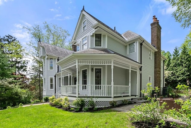victorian home with a chimney, a porch, a front lawn, and roof with shingles