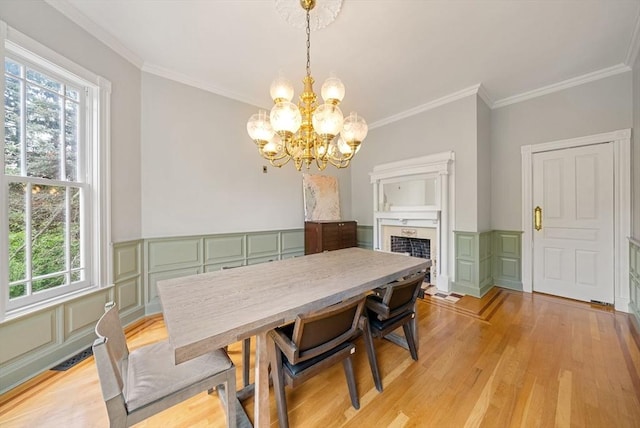 dining area with plenty of natural light, a chandelier, a decorative wall, light wood-style flooring, and crown molding