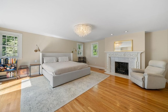 bedroom featuring multiple windows, light wood-style floors, a chandelier, and a high end fireplace