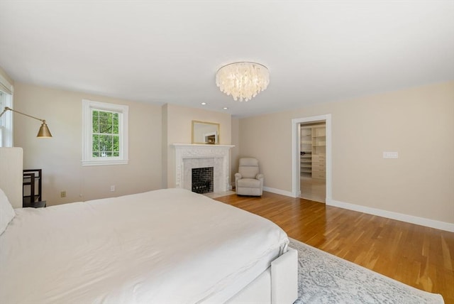 bedroom with wood finished floors, a chandelier, baseboards, and a fireplace with flush hearth