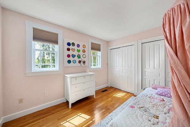 bedroom featuring baseboards, light wood-style floors, and two closets