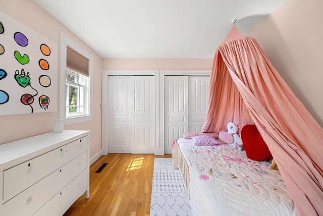 bedroom featuring multiple closets, light wood finished floors, and baseboards