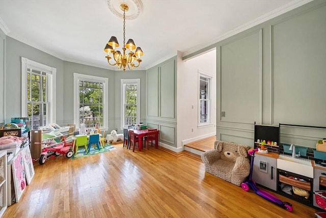 rec room with a decorative wall, a chandelier, light wood-type flooring, and ornamental molding