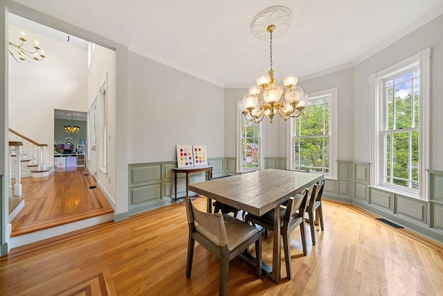 dining space featuring a chandelier, light wood finished floors, stairway, a decorative wall, and wainscoting