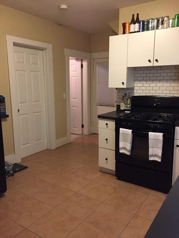 kitchen with light tile patterned floors, dark countertops, backsplash, black gas range oven, and white cabinets