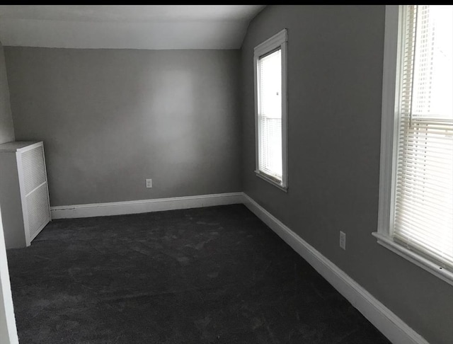 unfurnished room with vaulted ceiling, baseboards, and dark colored carpet