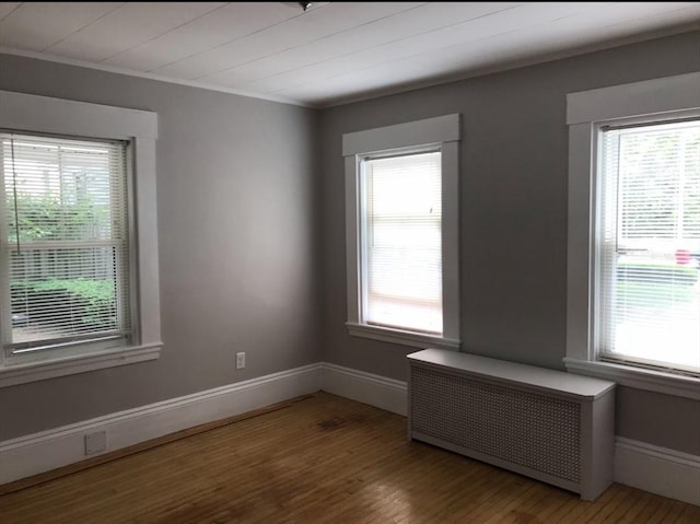 empty room featuring baseboards, wood finished floors, and radiator